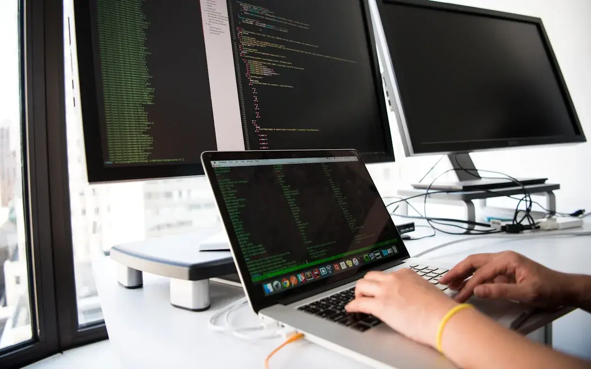 Werkplek met code op twee schermen terwijl er aan een website gebouwd wordt.